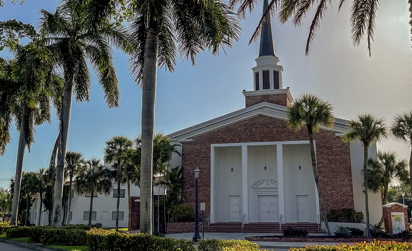 The white-columned facade and steeple of Grace Church Miami among palm trees